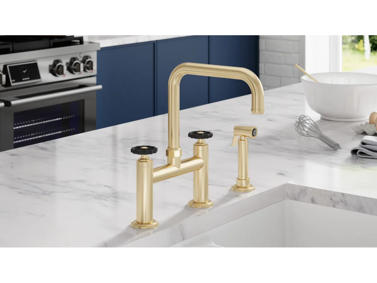 Modern kitchen faucet with gold finish on marble countertop next to stainless steel stove and blue cabinets.