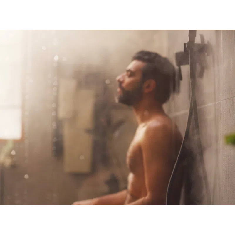 Man with beard enjoying a relaxing warm shower with steam and water droplets in a modern bathroom.