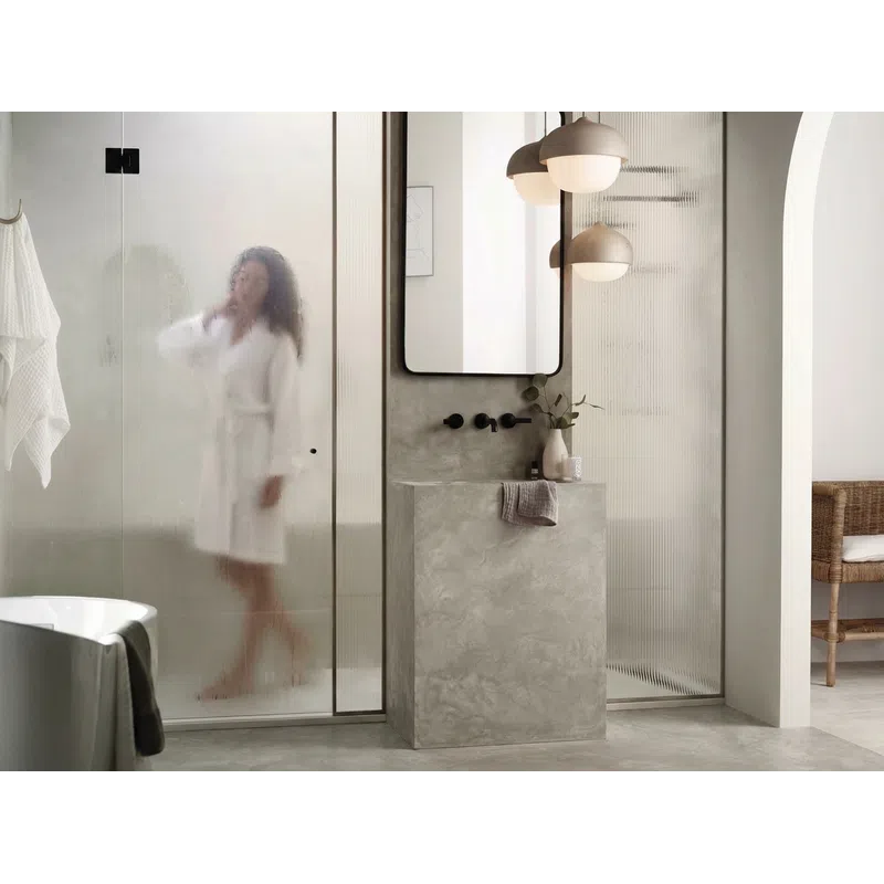Modern bathroom with textured glass shower, concrete sink, pendant lights, and a woman in a white robe.