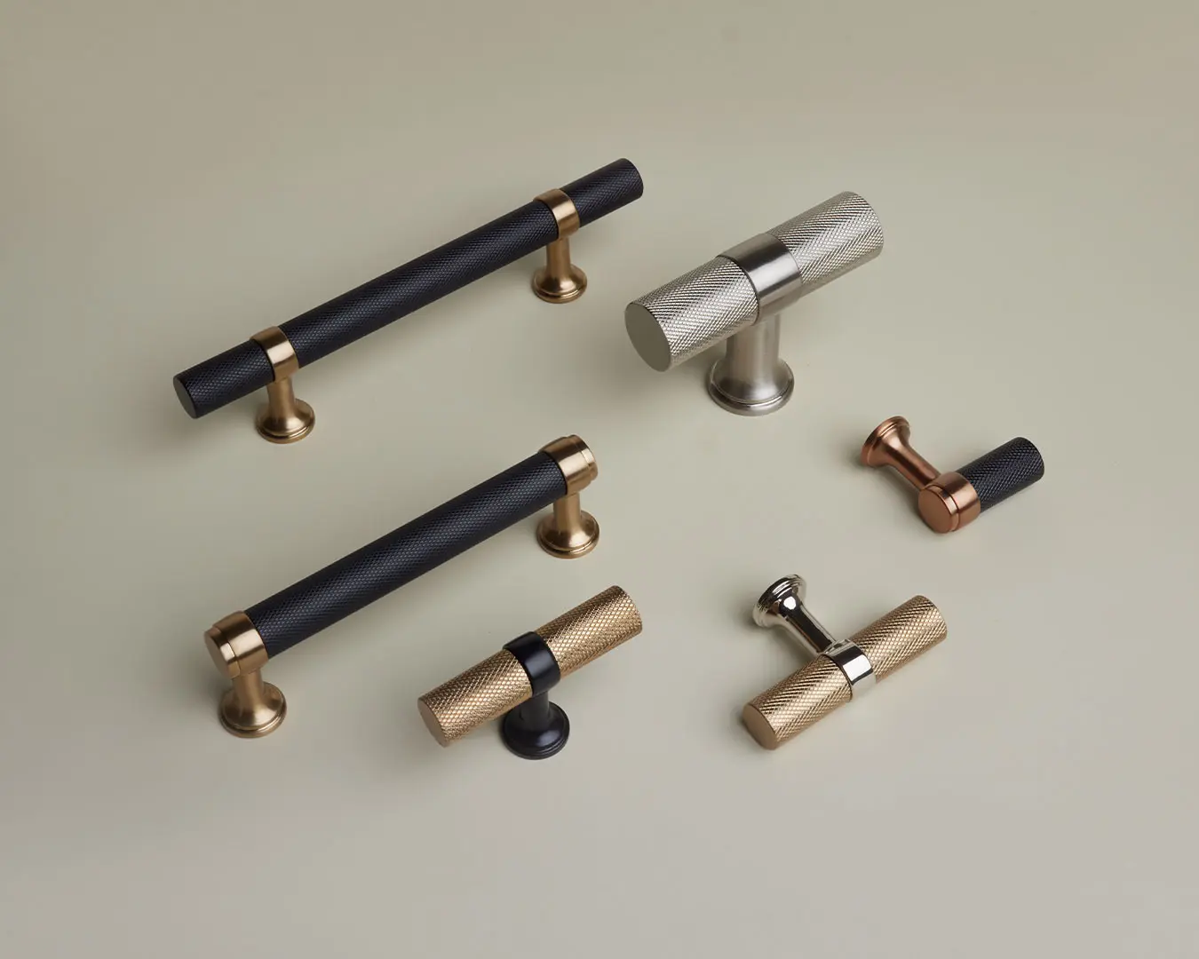 Assortment of designer cabinet knobs and door hardware pulls in black, brass, nickel, and bronze finishes on a neutral surface.