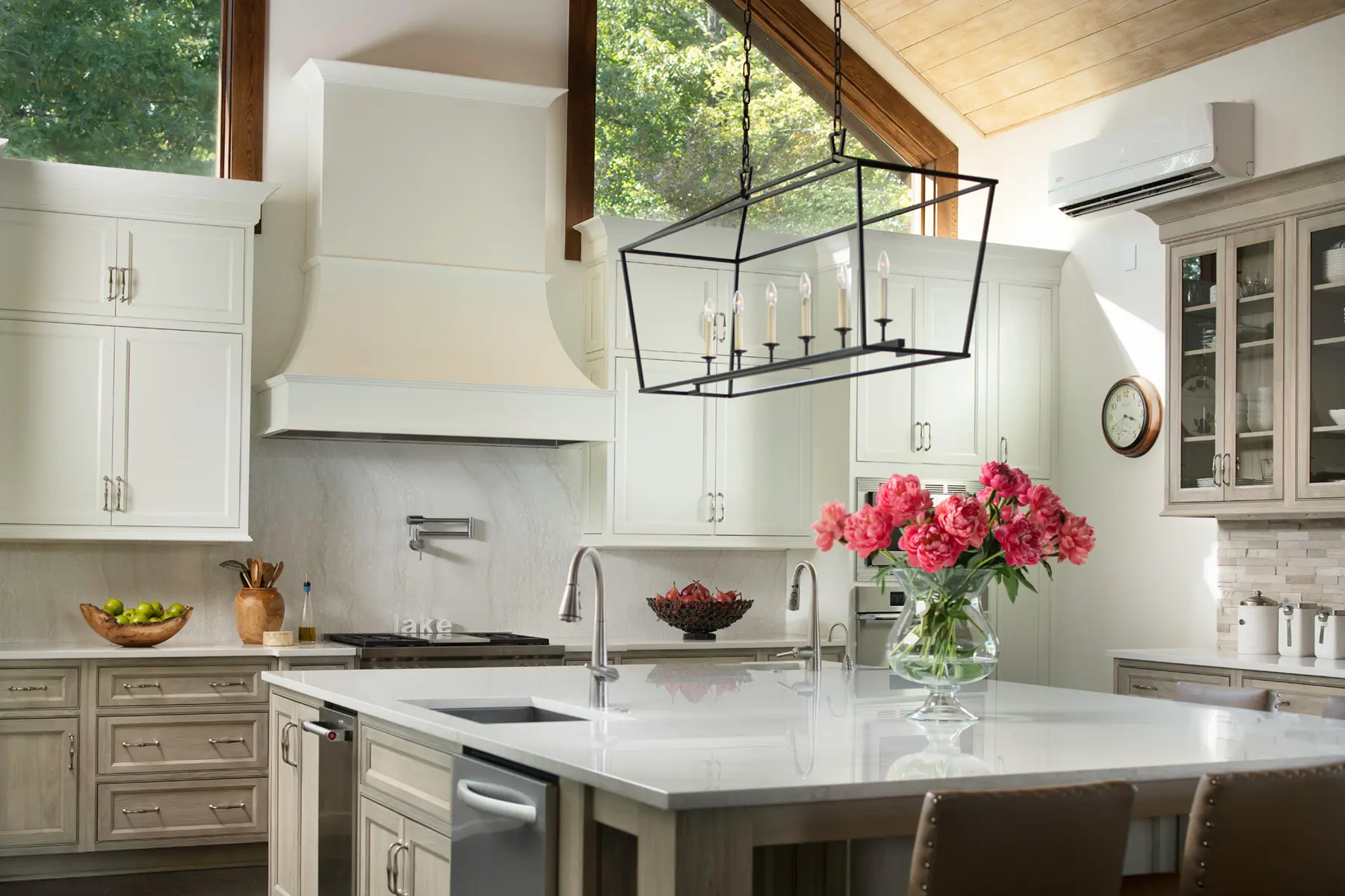Bright modern kitchen with white cabinetry, marble island, large windows, and pink flowers in vase on counter.