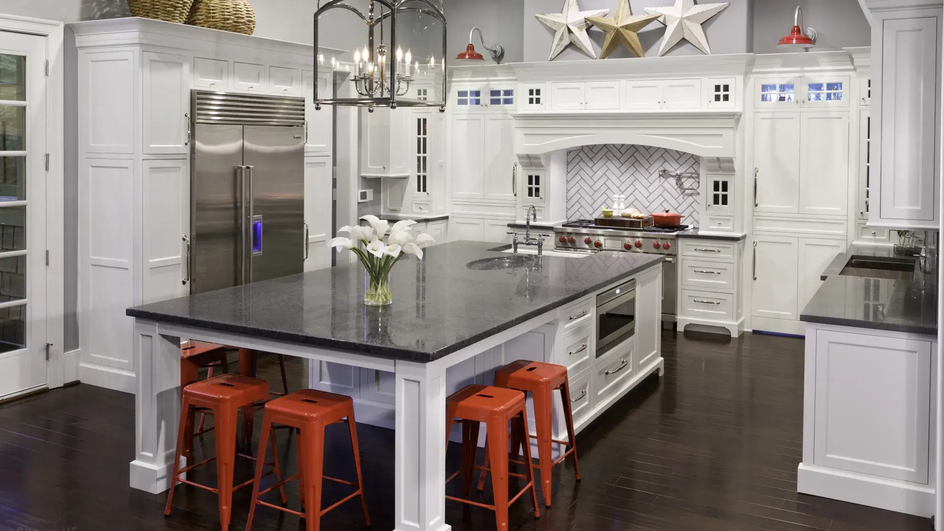 Modern kitchen with large white island, black countertop, red stools, stainless steel appliances, and star wall decor.