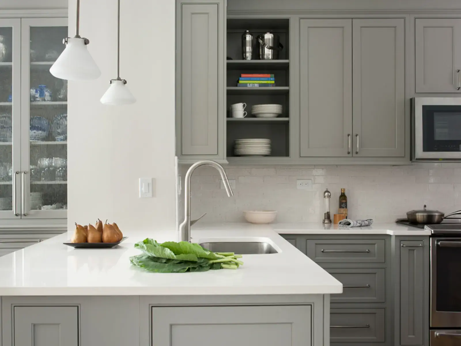 Modern gray kitchen with white quartz island, stainless steel appliances, pendant lights, and wooden floor.