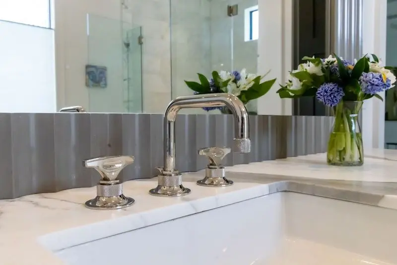 Modern bathroom faucet with stylish design and floral arrangement in the background.