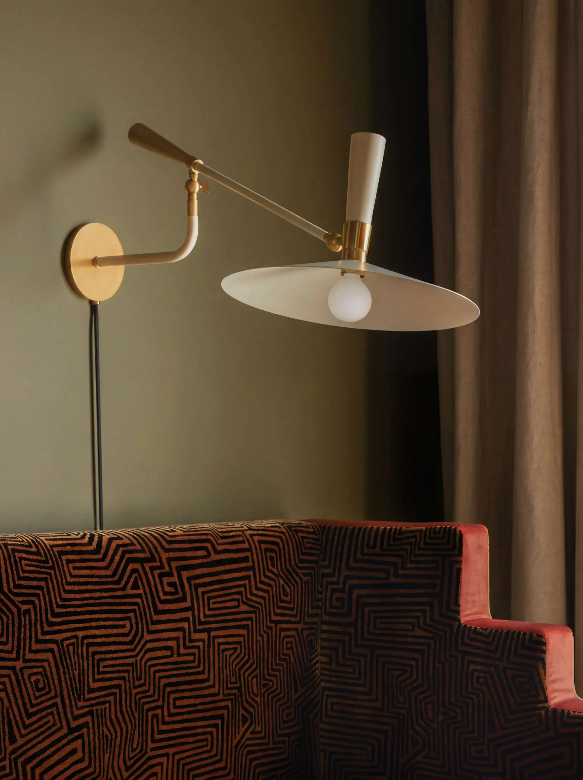 Brass and white articulating wall sconce with a fabric-shaded lamp above a patterned upholstered bench.