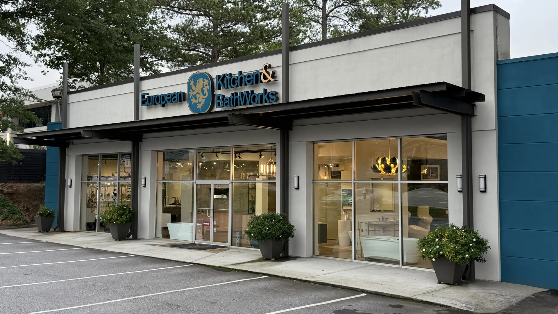European Kitchen & BathWorks storefront with large glass windows displaying kitchen and bath fixtures, and potted plants in front.