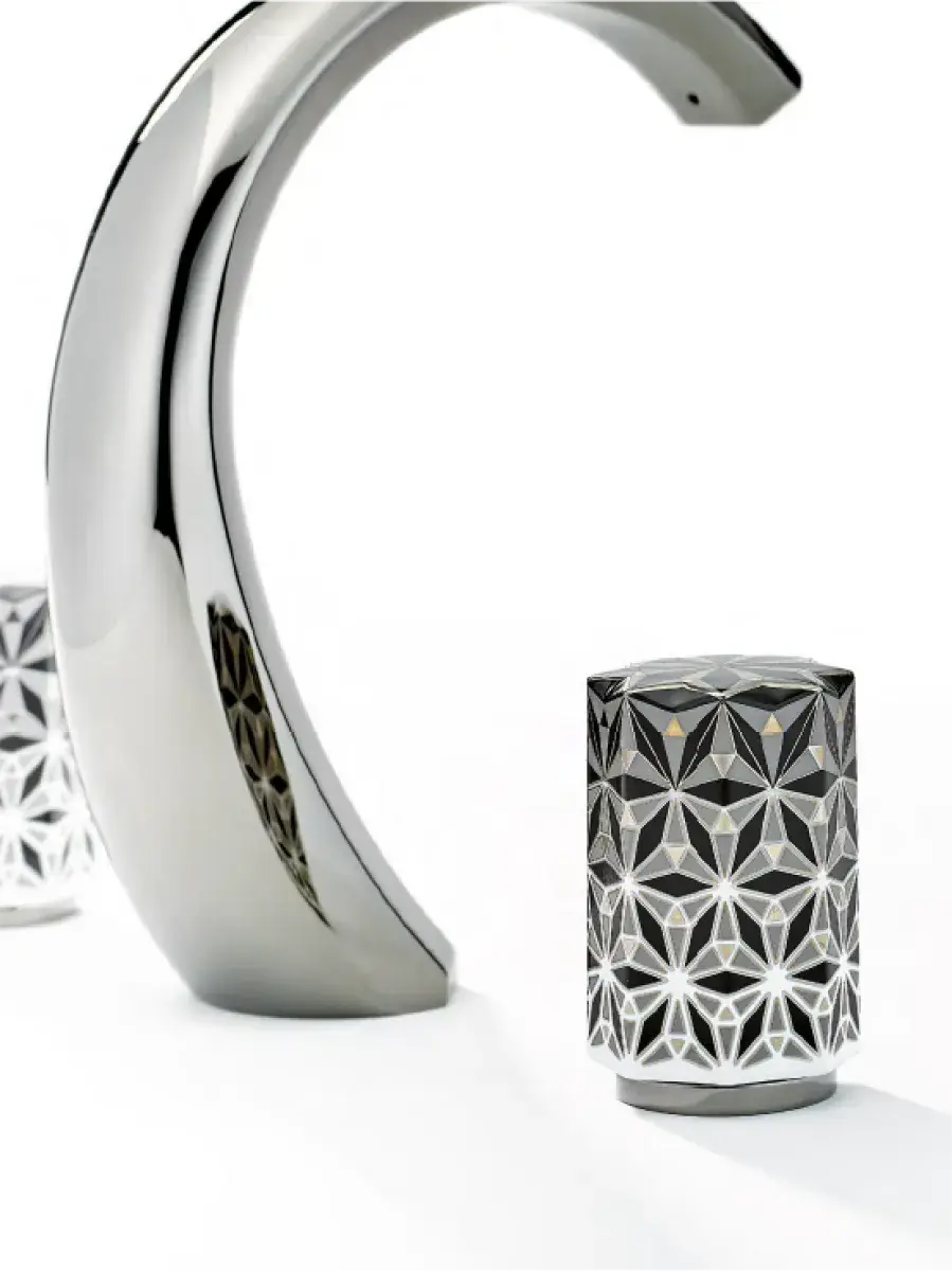 Polished chrome faucet handle with intricate geometric pattern against a white background.