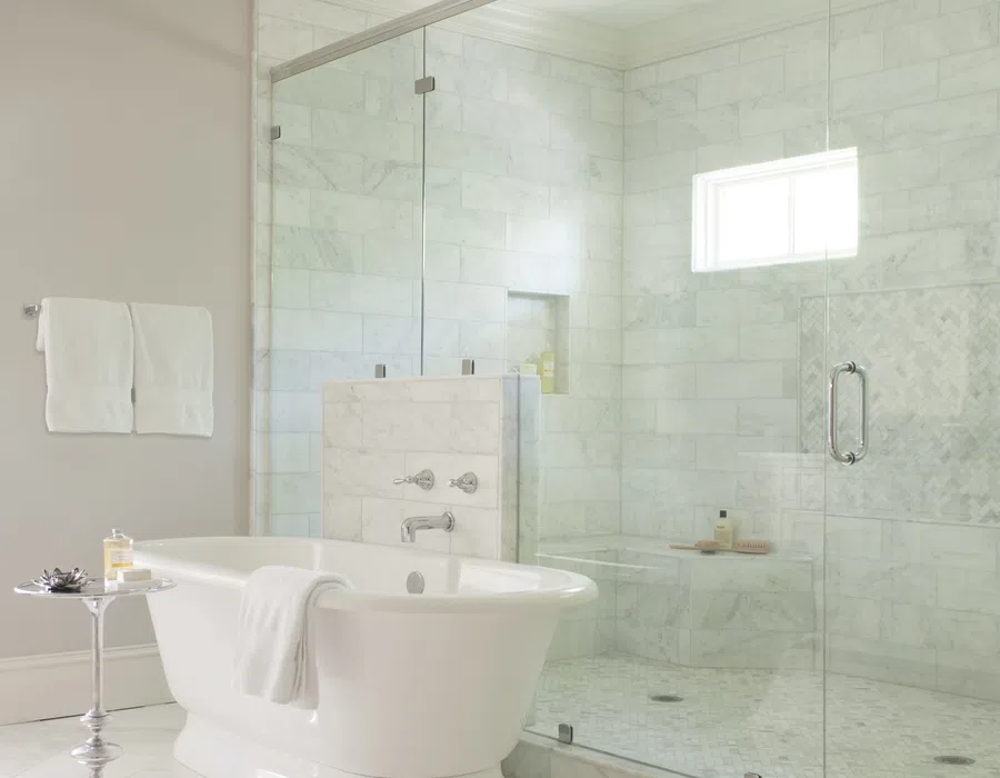Modern bathroom with white freestanding tub, glass shower enclosure, marble tiles, and soft natural light.