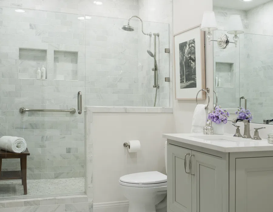 Bright modern bathroom with glass shower, white vanity, toilet, and decorative purple flowers on the counter.