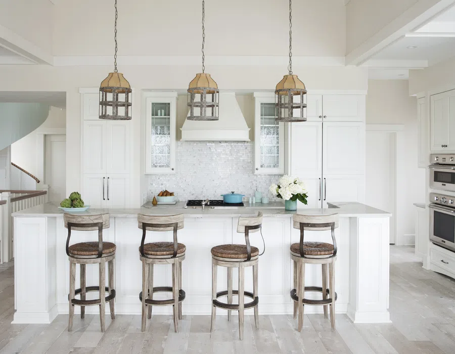Bright white kitchen with island seating, wooden bar stools, pendant lights, and stainless steel appliances.