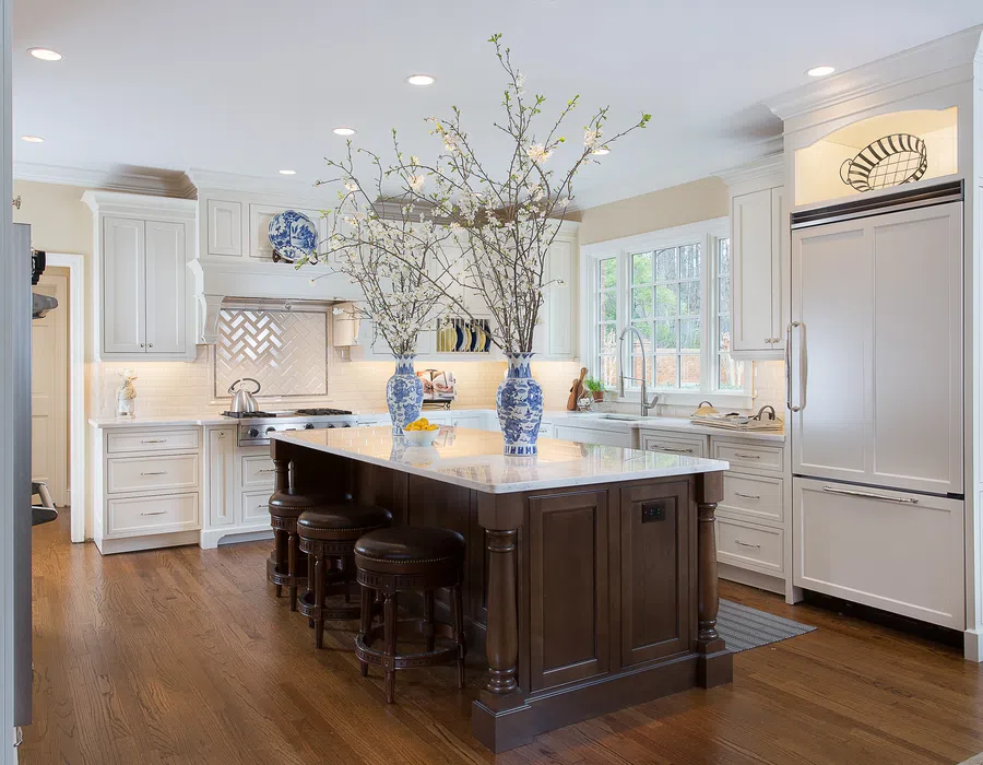 Bright kitchen with white cabinetry, dark wood island, marble countertop, and blue floral vases with branches.