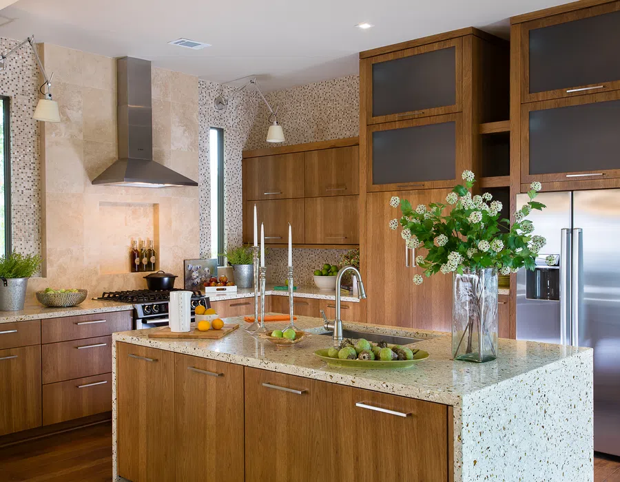 Modern kitchen with wood cabinets, terrazzo countertops, stainless steel appliances, and decorative plants.