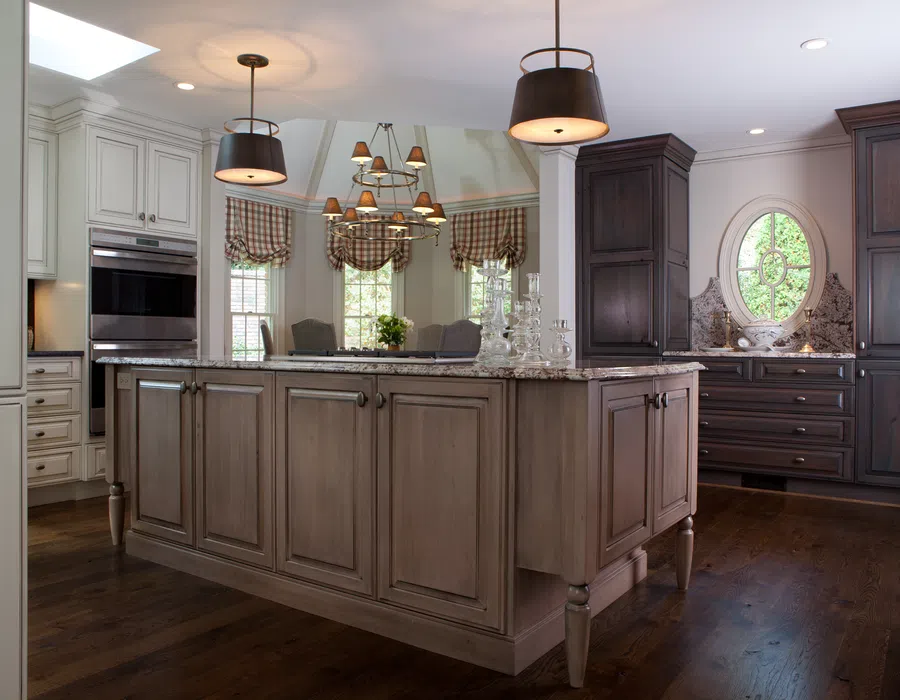 Spacious kitchen with central island, pendant lights, wooden cabinets, granite countertops, and oval window lighting.