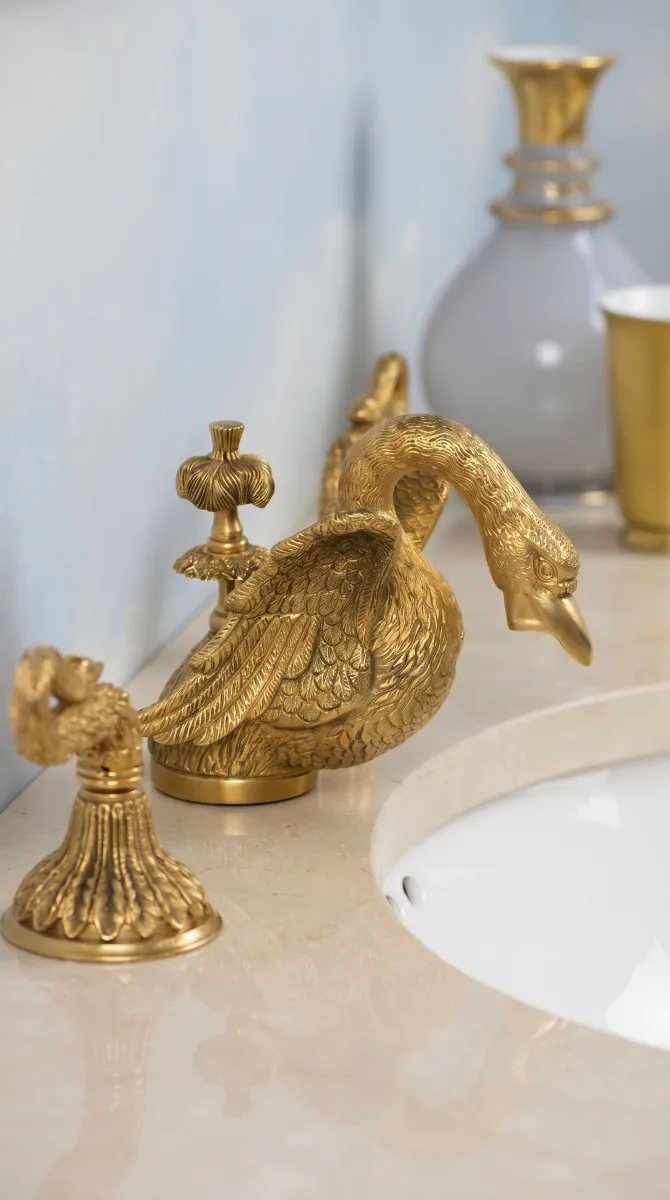Ornate hand-carved 24-karat gold Sherle Wagner swan faucet on a marble bathroom vanity.