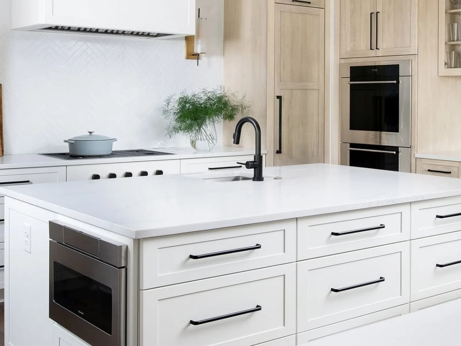 Modern white kitchen with large island, black hardware, built-in appliances, and minimalist decor