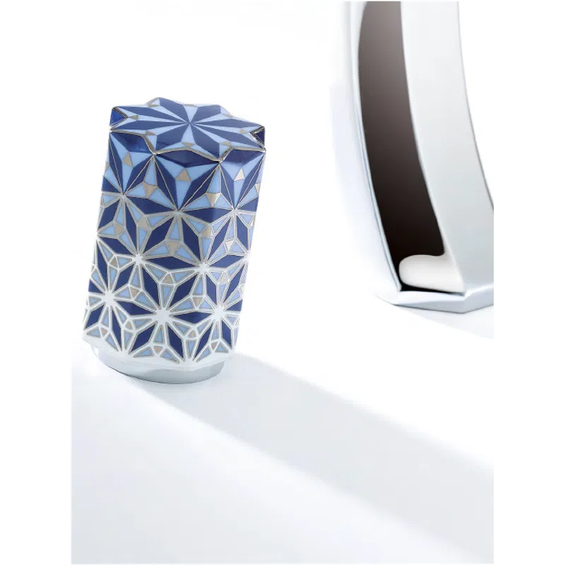 Blue and white geometric patterned vase with a star-shaped top next to a reflective metallic sculpture on white surface.