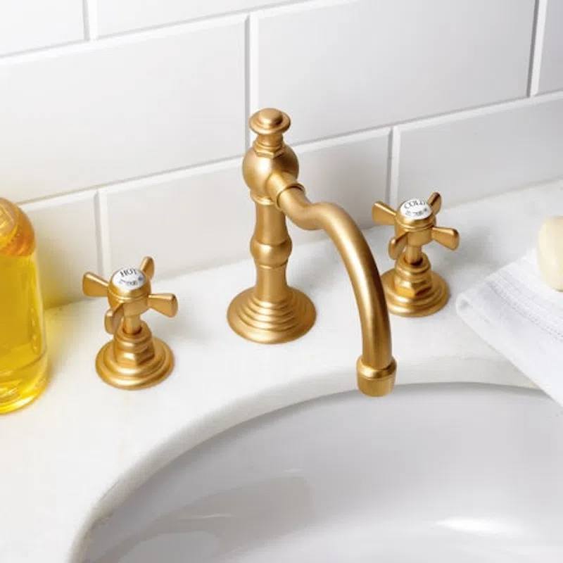 Brushed gold faucet with separate hot and cold handles on white bathroom sink with tiled wall background