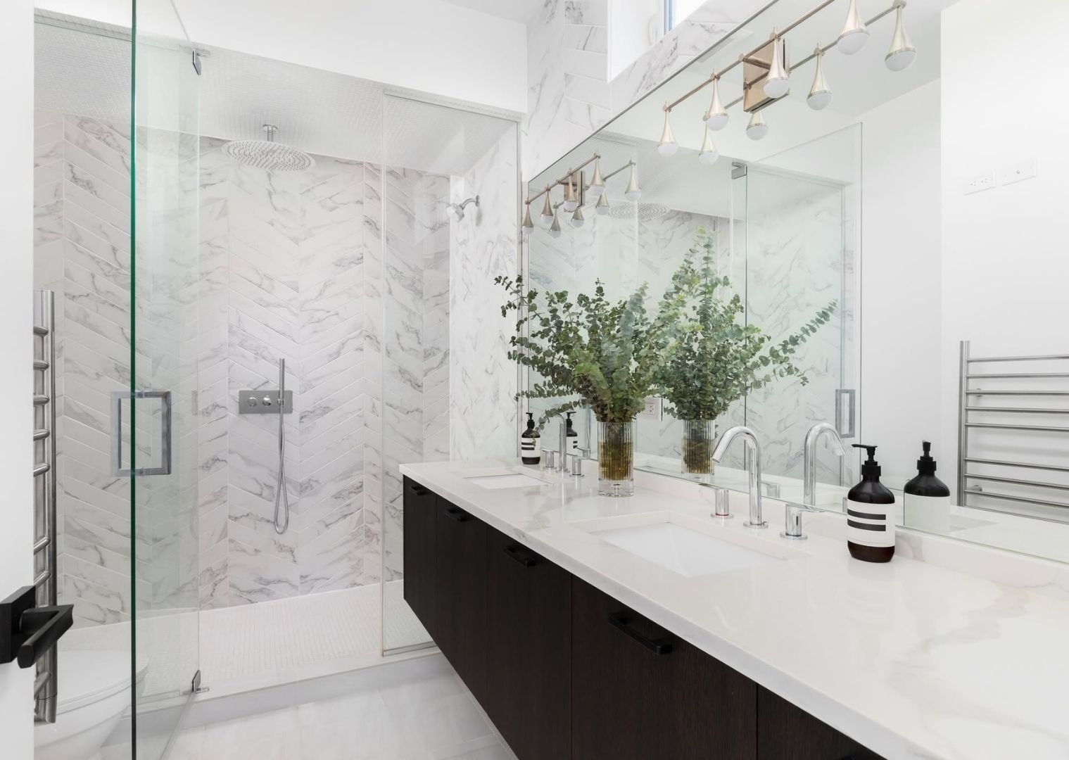 Modern bathroom with marble walls, glass shower, double sink vanity, and green plant centerpiece.