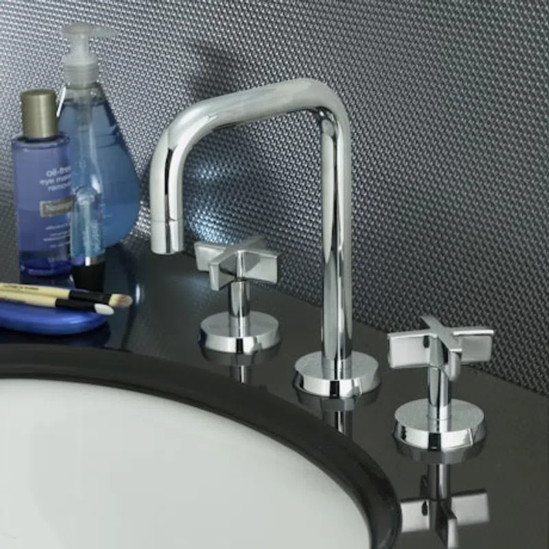 Modern chrome faucet with dual cross handles on a black countertop near skincare products and brushes